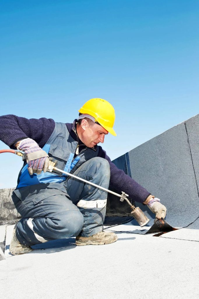 Worker finishing the construction of a commercial roof with the application of asphalt blanket.