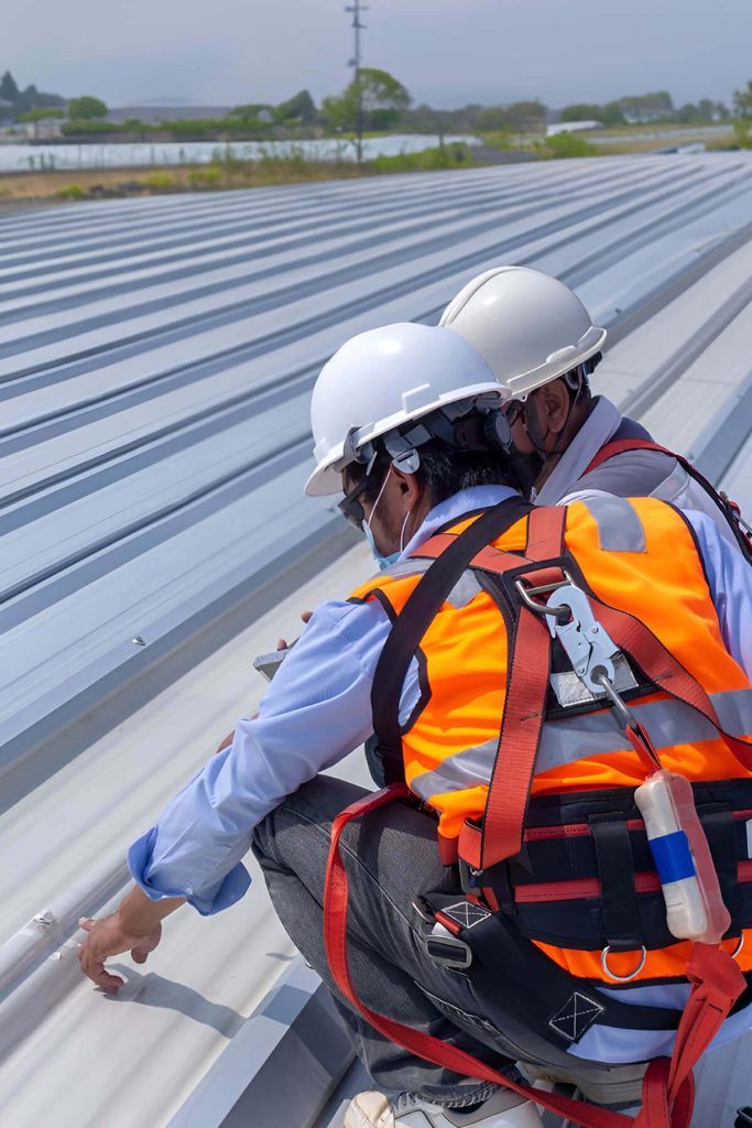 Two workers on top of a commercial metal roof checking for repairs.