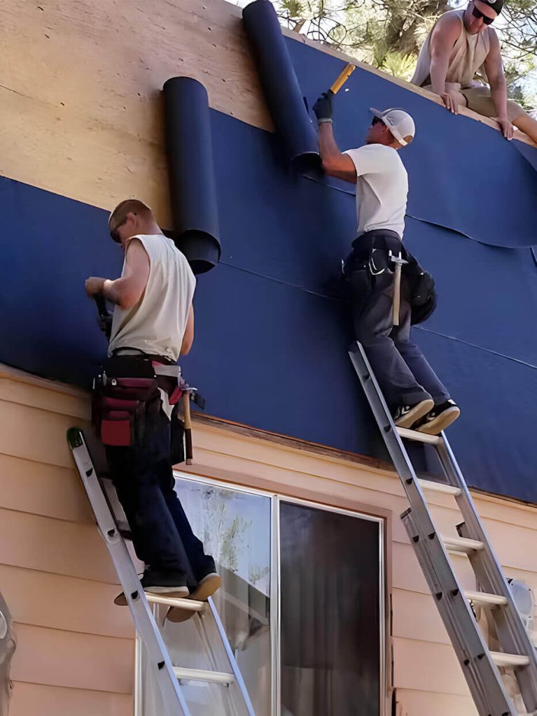 Two workers on ladders applying moisture protection blankets to the roof base.